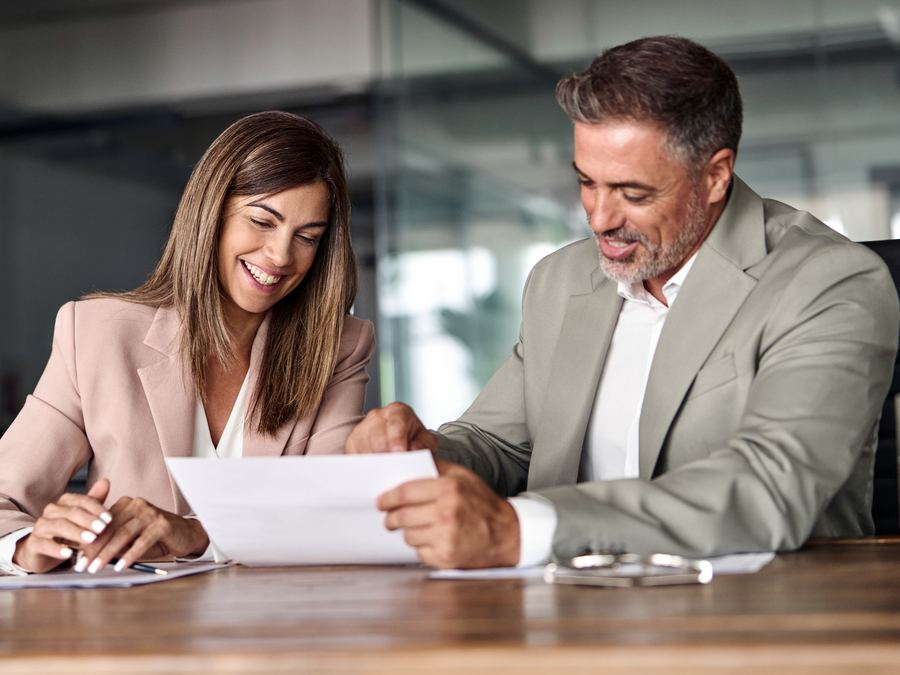 Dos personas leyendo juntas un documento y sonriendo